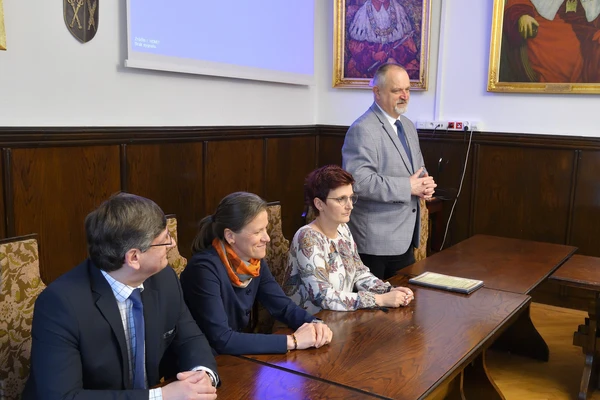 osoby siedzące za stołem i jedna osoba stojąca przemawiająca podczas spotkania podsumowującego Krakowskie Dni Integracji