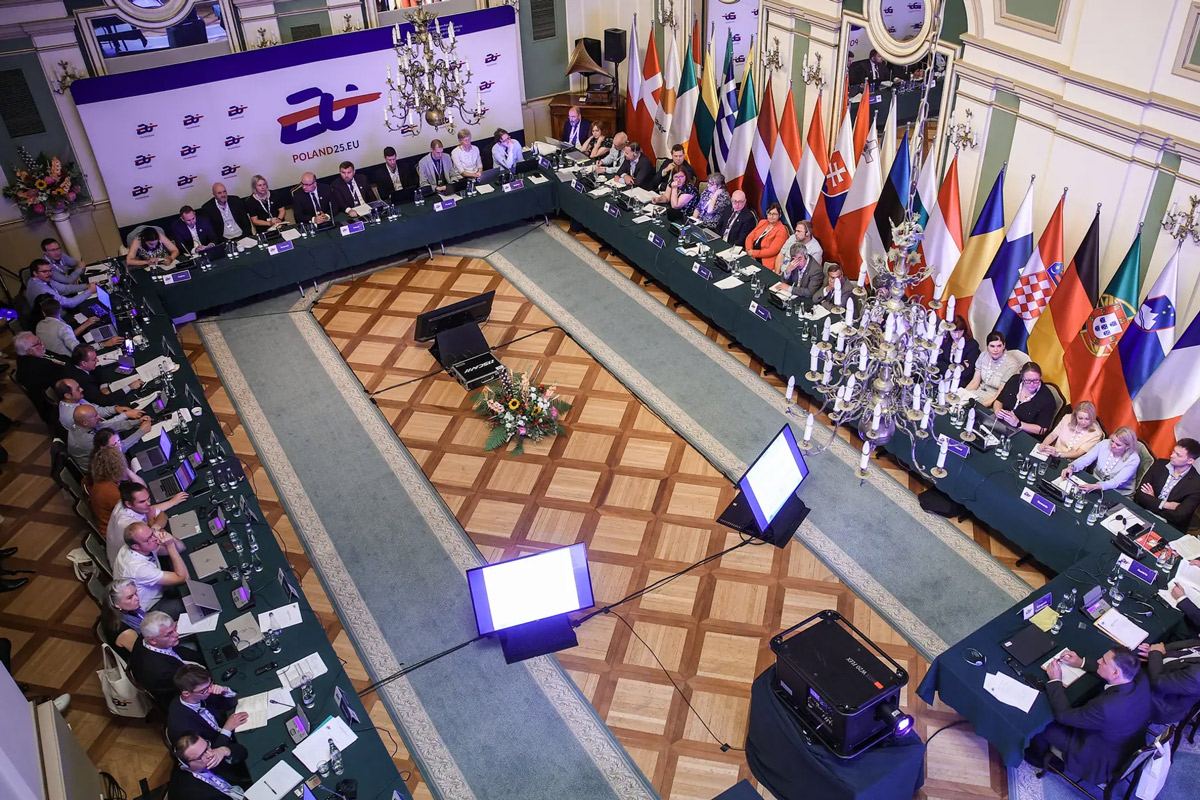 Sala obrad widoczna z góry. Pod ścianą ustawione flagi państw UE.