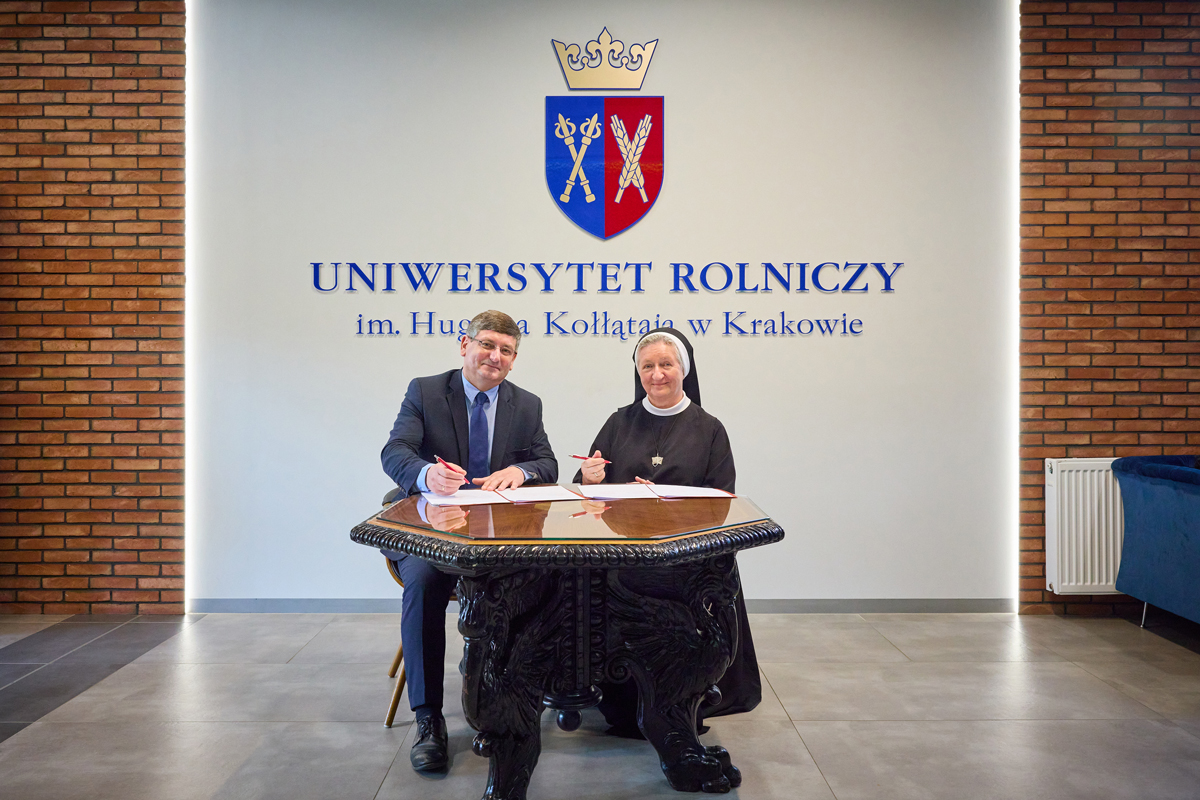 Na tle logotypu URK zdobiącego ścianę prorektor Bogdał i dyrektorka - s. Maria podpisują przy stoliku umowę.